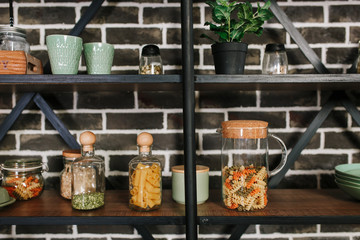 Black loft style storage stand with ceramic and wooden dishware in kitchen. Brick wall background