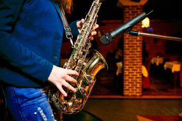 Fototapeta na wymiar hands of a girl dressed in jeans holding a saxophone near the microphone, playing on a saxophone