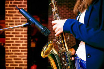 Fototapeta premium hands of a girl dressed in jeans holding a saxophone near the microphone, playing on a saxophone