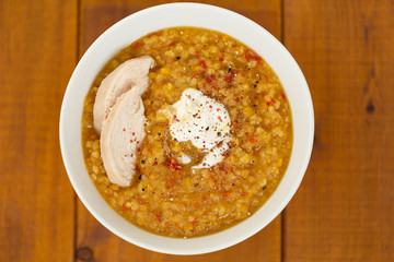 Turkish lentil bulgur soup sprinkled with pepper in a white bowl on a wooden background