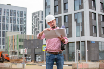 Portrait of architect at work with helmet in a construction site, reads the plan, paper projects