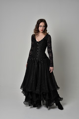 Naklejka premium full length portrait of brunette girl wearing long black gown with corset. standing pose on grey studio background.