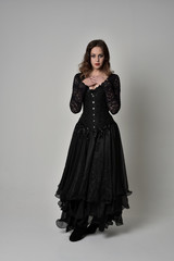 Fototapeta premium full length portrait of brunette girl wearing long black gown with corset. standing pose on grey studio background.