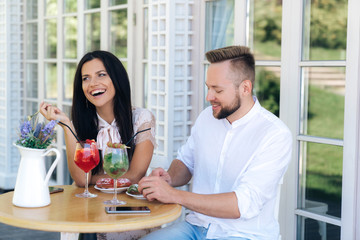 An attractive cheerful girl came to see a nice stylish guy. a couple is resting in a cafe, eating dies, talking and laughing. The woman has a European appearance.