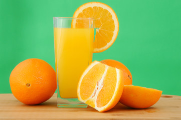 Glass of orange juice with slices of oranges on the green background
