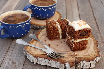 Pieces of carrot cake and two cups of coffee on a wooden background.
