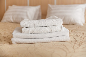 Fototapeta na wymiar Stack of white hotel towel on bed in bedroom interior.