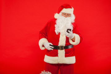 Photo of Santa Claus using mobile phone, on a red background. Ch