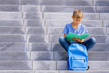 Boy sitting on the stairs and doing school homework.
