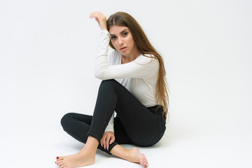 Fototapeta premium Studio portrait of a smiling happy beautiful brunette girl on a white background talking and sitting on the floor.