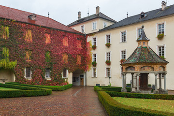 Inner yard of a building with a wall fully covered by bright vivid colourful saturated multicoloured leaves of creeping ivy seen in autumn in Italy, South Tyrol. Foliage in red, green, orange, yellow.