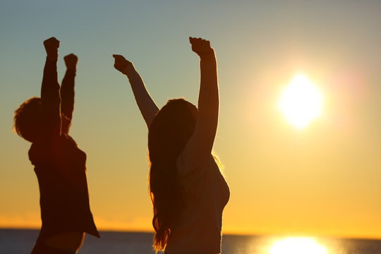 Excited friends raising arms at sunset on the beach