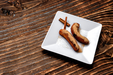 fried banana served on white square plate with cinnamon and sugar, over dark wood