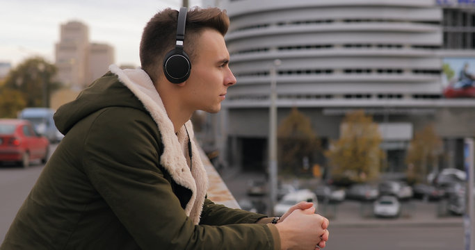 Young man listening to music in headphones at city bridge and thinking