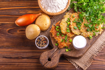 Homemade traditional potato pancakes Hanukkah celebration food with ingredients on vintage cutting board. Rustic wooden background. Horizontal view