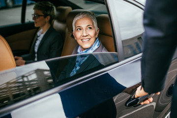 Senior business woman and her assistant sitting in limousine talking and working. - obrazy, fototapety, plakaty