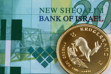 A macro image of a gold one ounce krugerrand with a 20 Israeli bill close up