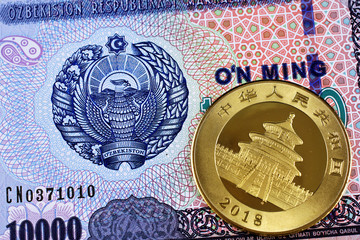 A macro image of an Uzbek ten thousand som bank note with a gold Chinese one ounce panda coin