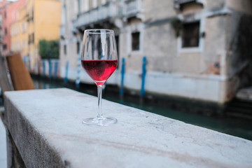 A glass of red wine standing on the parapet of the canal embankment in Venice