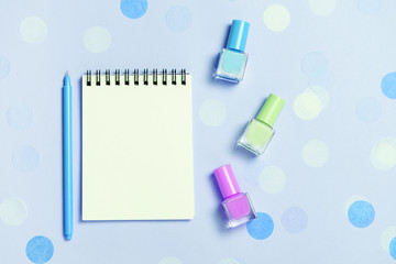 Empty note pad and colorful nail polishes on blue confetti background.