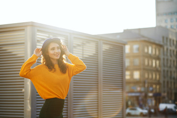 Street portrait of beautiful girl wearing blue hat and yellow knitted sweater posing in sun rays. Space for text