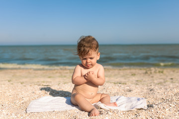 little child sitting on a towel by the sea naked cheerful and happy