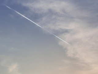 White trail from the aircraft's engines in blue sky. Cloudly.