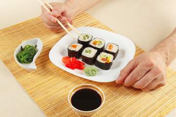 Hands taking sushi with chopsticks. Sushi set with ginger and wasabi on a bamboo mat.