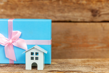 Miniature white toy house and gift box wrapped blue paper on old shabby rustic wooden background. Mortgage property insurance dream home concept. Buying new house for family