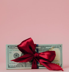 one hundred dollars gift wraped with a red ribbon on pink background