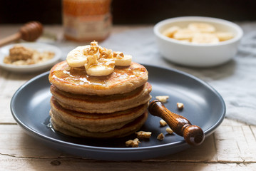 Pancakes with banana, nuts and honey, served with tea. Rustic style.