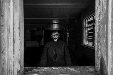 Unknown person with creepy horrible latex mask looking out from old wooden ghost house window....