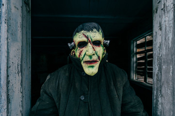 Unknown person with creepy horrible latex mask looking out from old wooden ghost house window....