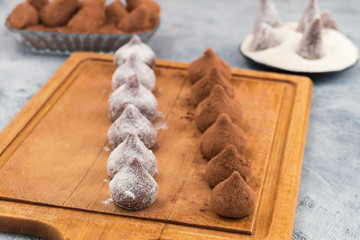 Two rows of chocolate truffles with brown and white powder on the kitchen Board.