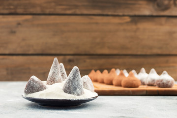 Chocolate candies in a round plate with powdered white sugar powder, wooden background, copy space.