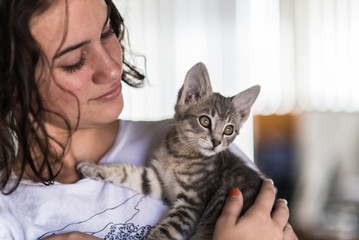 Loveable grey tabby kitten being held with love as teenage girl looks down at him.