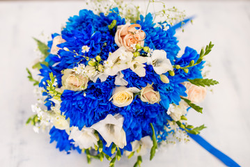 Beautiful modern wedding bouquet of blue chrysanthemum, freesia, roses and peony. on white wooden background. With rings newlyweds