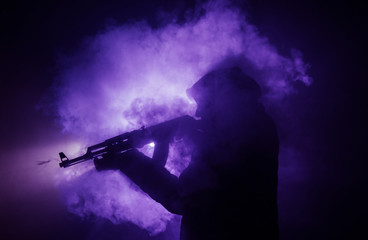 Silhouette of man with assault rifle ready to attack on dark toned foggy background or dangerous...