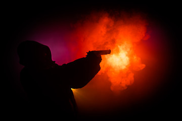 Silhouette of man with assault rifle ready to attack on dark toned foggy background or dangerous...