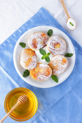 Cottage cheese pancakes sprinkled powdered sugar and fresh mint. Cheesecakes on white plate. Sour cream in wooden spoon. Honey and dairy products on white blue background. Healthy food