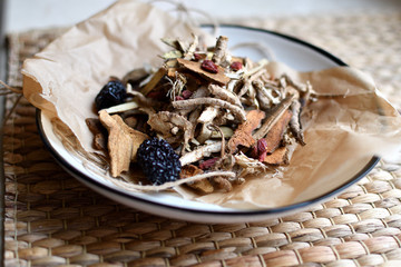 Chinese traditional medicine script. Herbal tea with jujubes, goji berries, gingseng roots and others on parchment paper on neutral background.