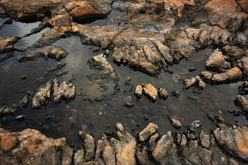 smooth dark water reflecting the leaden sky in the hollows of hardened lava covered with rusty patina