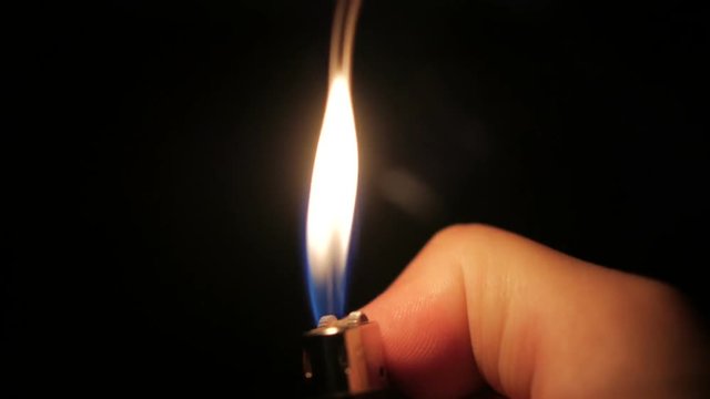 Flame lighter on a black background. A hand holding a fireburner.
