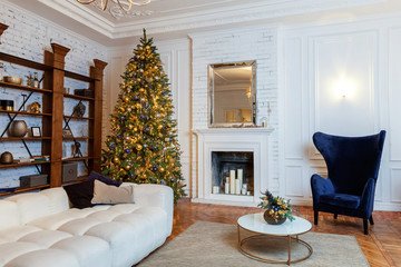 Classic Christmas decorated interior room New year tree. Christmas tree with gold decorations. Modern white classical style interior design apartment with fireplace and armchair. Christmas eve at home