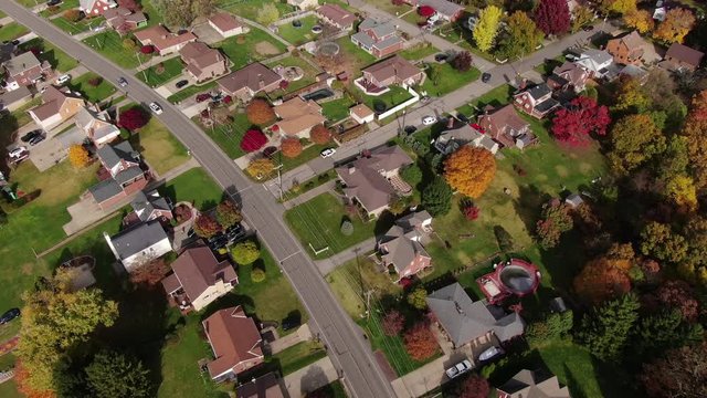 A reverse aerial flyover establishing shot of a typical Pennsylvania residential neighborhood in the late Autumn. Modest homes nestled in Fall foliage below. Pittsburgh suburbs.  	