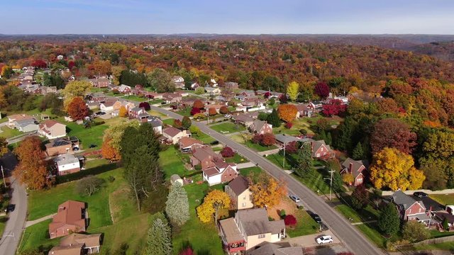A forward aerial flyover establishing shot of a typical Pennsylvania residential neighborhood in the late Autumn. Modest homes nestled in Fall foliage below. Pittsburgh suburbs.  	