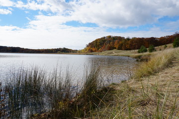 Fall landscape in the Midwest with lake, clouds, and grass with fall leaves on trees