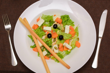 Salad of pumpkin, salad, pumpkin seeds, olives, meat on a white plate