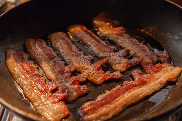 Bacon strips or rashers cooked in frying pan in the rays of sunlight