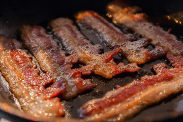 Bacon strips or rashers cooked in frying pan in the rays of sunlight. Close-up